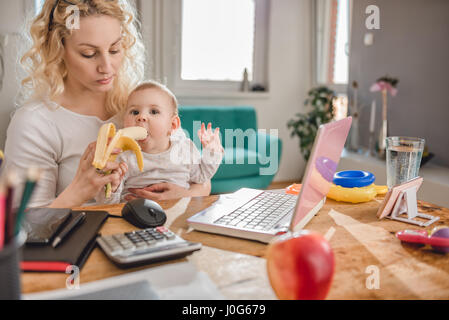 Mère nourrir bébé au bureau à domicile avec des bananes Banque D'Images