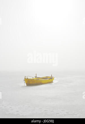 Bateau jaune piégés dans lac gelé en Matin brumeux Banque D'Images