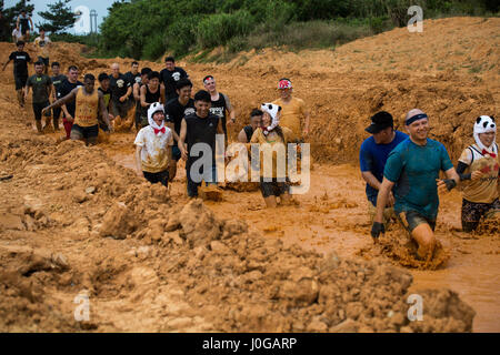Les Marines et les participants locaux naviguent dans une fosse à boue lors de la course annuelle Camp Hansen Mud Run à Okinawa, au Japon, s'engageant dans une activité récréative et de consolidation d'équipe. Banque D'Images