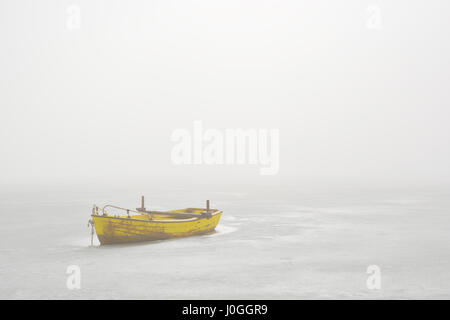 Bateau jaune piégés dans lac gelé en Matin brumeux Banque D'Images