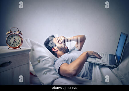 Homme fatigué working on laptop in bed Banque D'Images