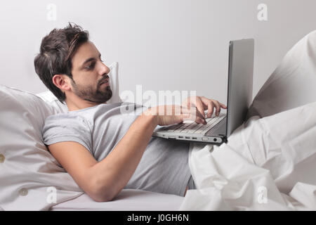 Man working on laptop in bed Banque D'Images