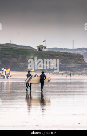 Gwithian Towans beach deux surfeurs hommes marcher dans la mer la mer transportant des planches de l'autre activité de loisirs vacanciers Longboards côtières Banque D'Images