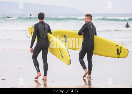 Gwithian Towans beach deux surfeurs hommes marcher dans la mer la mer transportant des planches de l'autre activité de loisirs vacanciers Longboards côtières Banque D'Images