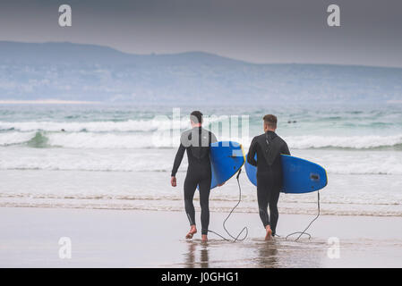 Gwithian Towans beach ; deux hommes surf ; marcher dans la mer, Mer, transportant des planches ; littoral ; littoral ; ; ; les vacanciers Longboards activité de loisirs Banque D'Images