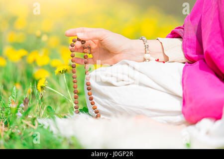 Femme lit le mantra yoga pendant la pratique avec la mala sur une prairie fleurie au printemps Banque D'Images
