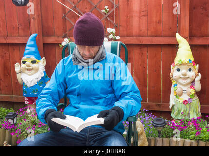 Livre de lecture de l'homme dans le jardin avec gnomes en arrière-plan. Banque D'Images