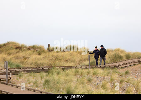 Un homme et une femme marchant le long d'une promenade de bois construit à cet effet à travers les dunes de sable de la station balnéaire populaire et plage de la ville de Muro dans le Nord du Pays de Galles Banque D'Images