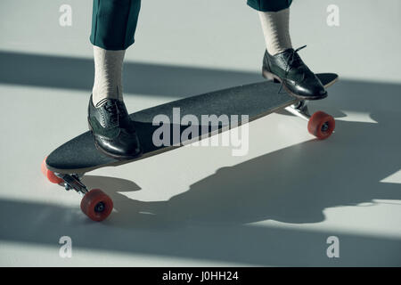 Les jambes des femmes dans des chaussures noires debout sur skateboard avec ombres sur marbre blanc Banque D'Images