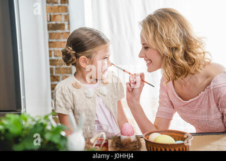 Jeune mère et son joli fille s'amusant tout en peignant des œufs pour Pâques Banque D'Images