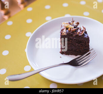 Tranche de gâteau au chocolat servi sur une plaque blanche avec nappe à pois jaune Banque D'Images