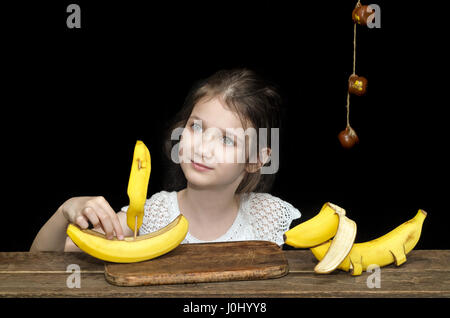 Petite fille et des jouets à partir de la banane, voile et le chien. Fond noir. Banque D'Images