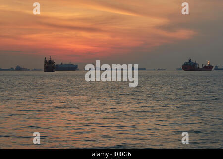 Le lever du soleil sur les navires à l'ancre dans le détroit de Singapour. Banque D'Images