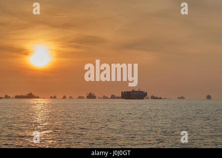 Le lever du soleil sur les navires à l'ancre dans le détroit de Singapour. Banque D'Images