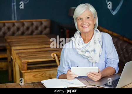 Portrait of smiling senior woman holding digital tablet while sitting at table in cafe shop Banque D'Images