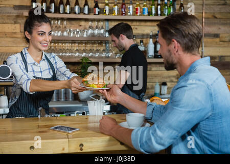 Serveuse servant le petit-déjeuner à l'homme au comptoir de cafe Banque D'Images