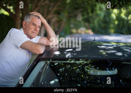 Tendu senior man with head in hand leaning on car Banque D'Images