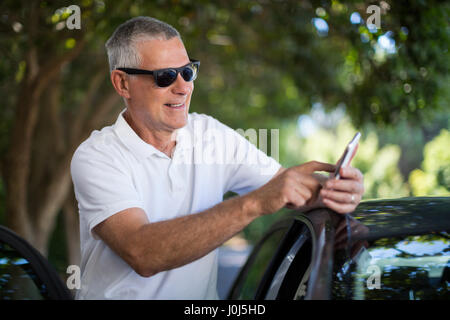 Smiling senior man using smart phone en position debout en voiture Banque D'Images