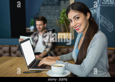 Portrait of young woman using laptop while having coffee in café