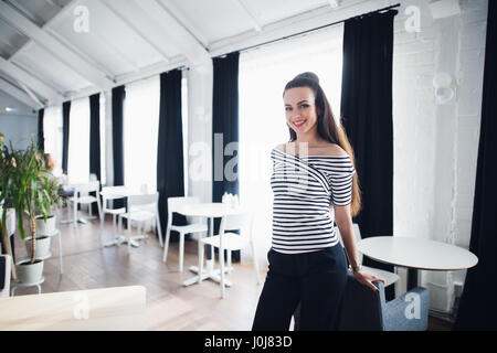 Portrait d'une belle femme regardant la caméra près de la fenêtre. Café adultes propriétaire avec un sourire accueillant dans un intérieur moderne Banque D'Images
