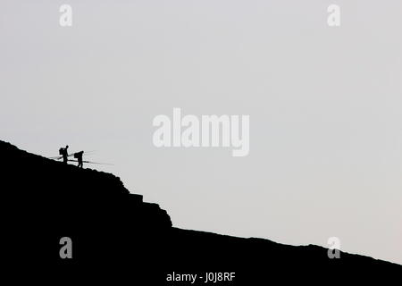 Une photo de deux (2) pêcheurs sur une falaise, silhouetté contre un ciel gris du plan. L'espace de copie, pêche, hobby, détente concept. Banque D'Images