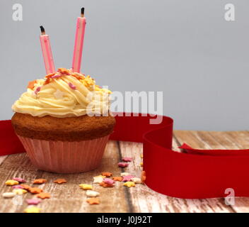 Celebration cupcake avec crème au beurre, du ruban rouge cerise, Rose et deux bougies en forme d'asperge Banque D'Images