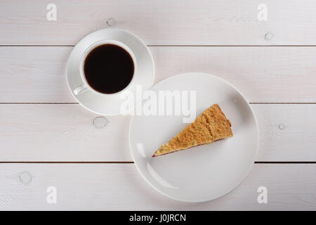 Une tasse de café noir et un morceau de tarte aux petits fruits savoureux sur un pied à platine sur une table en bois blanc. Vue d'en haut Banque D'Images