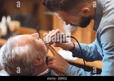 Coiffure charismatique barbe en forme du client dans le barbershop Banque D'Images