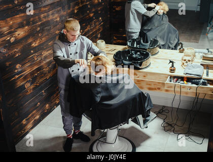 Petit garçon se coupe par coiffure While Sitting in Chair At Barbershop. Thème Barbershop Banque D'Images