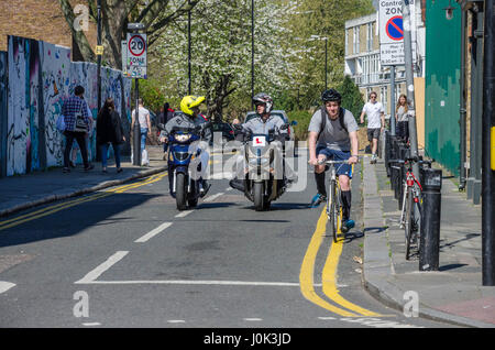 Un cycliste et un couple de fauteuils motorisés sur Brick Lane dans l'Est de Londres. Banque D'Images