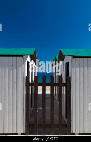 Concept d'été vert et blanc pur avec des cabines de plage derrière une clôture en recul de deux lignes menant à une plage de sable et l'océan sur un sunny blue Banque D'Images
