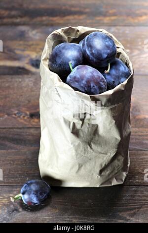 Damson prunes dans un sac en papier isolé sur fond de bois Banque D'Images