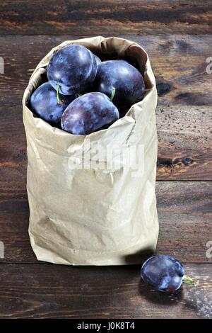 Damson prunes dans un sac en papier isolé sur fond de bois Banque D'Images