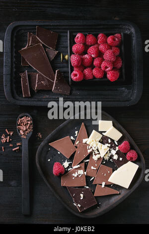 Variété de noir, au lait et blanc Hacher le chocolat sur plaque ancienne et la cuillère avec les framboises en bois noir fort sur fond de bois brûlé noir. Banque D'Images