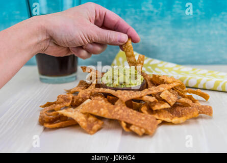 La main gauche va à tremper une puce dans le guacamole avec des wonton chip Banque D'Images