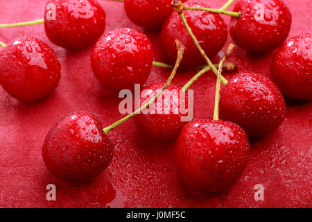 Les cerises douces humide sur fond textile peint rouge Banque D'Images