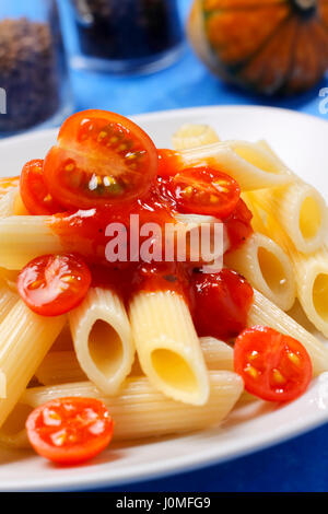 Les pâtes (penne) avec une sauce tomate et tomates cocktail de moitié sur la plaque Banque D'Images