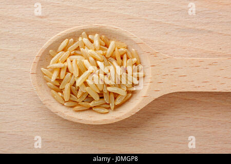 Cuillère en bois remplis de grains de riz brun. Close-up, vue du dessus. Banque D'Images