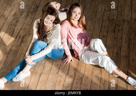 Trois belles jeunes femmes souriant assis ensemble sur plancher en bois Banque D'Images