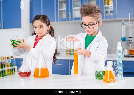 Petits enfants concentrés dans un sarrau de laboratoire chimique dans l'expérience de décisions Banque D'Images