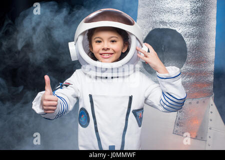 Jolie petite fille en costume d'astronaute showing thumb up and smiling at camera Banque D'Images