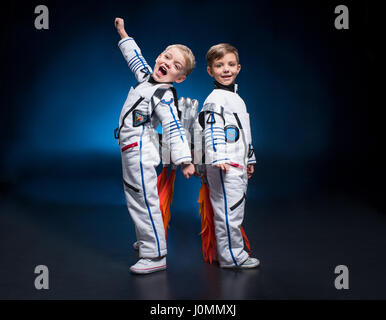 Deux adorables petits garçons dans les combinaisons spatiales standing back to back looking at camera Banque D'Images