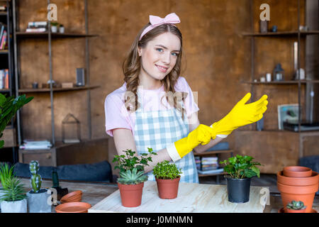 Belle jeune femme souriante portant des gants de caoutchouc avec des plantes en pots sur table en bois Banque D'Images