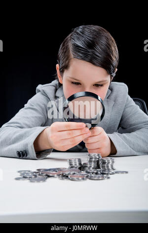 Portrait de garçon à la recherche de pièces de monnaie à travers une loupe sur black Banque D'Images