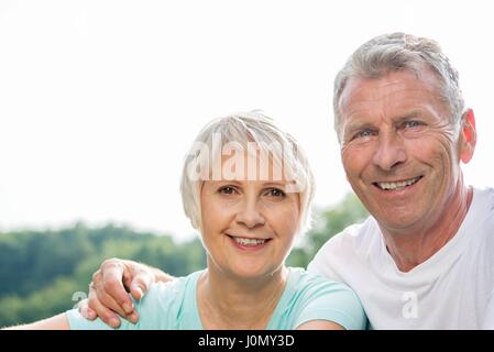 Senior couple smiling vers la caméra, l'homme avec le bras autour de la femme. Banque D'Images