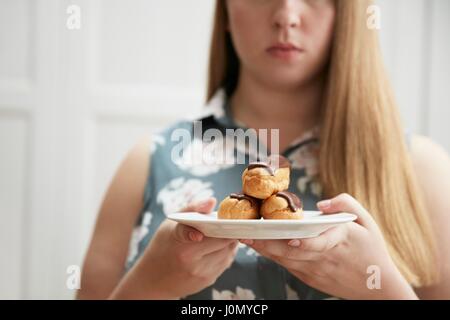 Jeune femme maintenant la plaque d'éclairs au chocolat. Banque D'Images