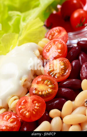 Salade de légumes close-up. Haricots blancs et rouges, tomates cerises, des pâtes, de la laitue et la crème. Banque D'Images