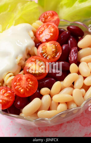 Salade de légumes dans un bol. Haricots blancs et rouges, tomates cerises, des pâtes, de la laitue et la crème. Banque D'Images