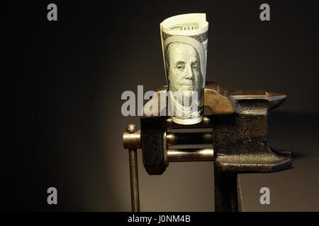 Problème de l'économie.One hundred dollar bill fait pression sur dans un étau sur fond sombre Banque D'Images
