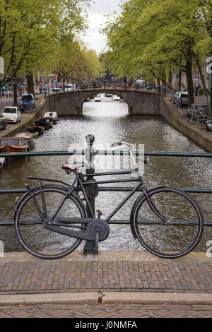 Un vélo hollandais en stationnement sur un pont avec le Reguliersgracht en arrière-plan, Amsterdam, l'Europe. Banque D'Images